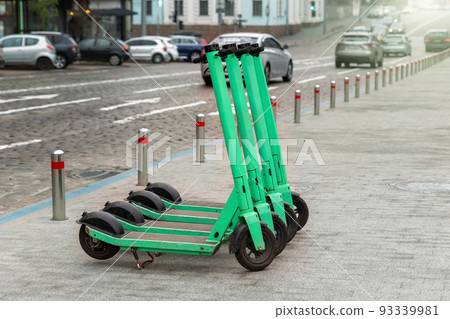 Many modern green electric scooters sharing parked city street. Self-service street transport rental service. Rent urban mobility vehicle with smartphone application. Zero emission green eco energy 93339981
