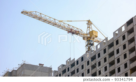 High yellow crane over the building construction. Blue sky background. 93341794