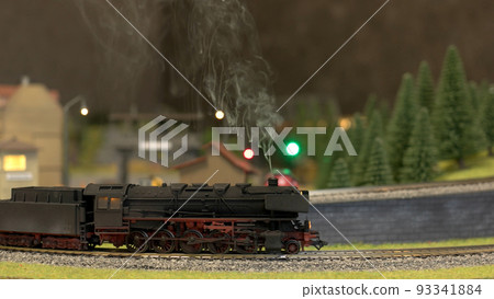 A model train running along tracks outdoors in forest. A model of a train moves down the miniature railroad. A model train running along tracks outdoors in forest. A model of a train moves down the miniature railroad. 93341884