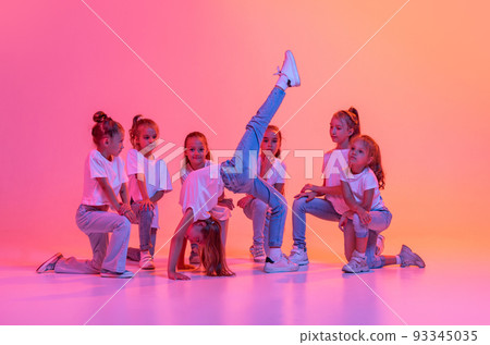 Group of children, school age girls in sportive casual style clothes dancing in choreography class isolated on pink background in yellow neon light. Group of children, school age girls in sportive casual style clothes dancing in choreography class isolated on pink background in yellow neon light. 93345035