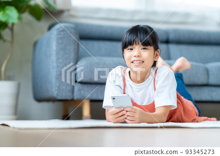 Elementary school girl using a smartphone in the living room Elementary school girl using a smartphone in the living room 93345273