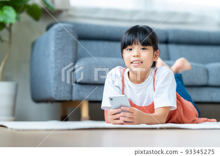 Elementary school girl using a smartphone in the living room Elementary school girl using a smartphone in the living room 93345275