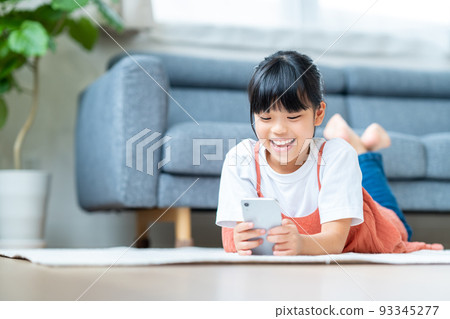 Elementary school girl using a smartphone in the living room Elementary school girl using a smartphone in the living room 93345277
