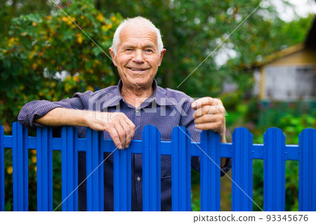 Portrait of pensive elderly man at fence of his country house in village 93345676