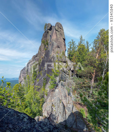 200-foot rock formation in the forest. Erosion of rocks. Unrecognizable mountaineer is climbing to top of the rock without climbing protection. 200-foot rock formation in the forest. Erosion of rocks. Unrecognizable mountaineer is climbing to top of the rock without climbing protection. 93345840