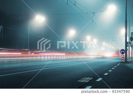 View empty dark night blue foggy misty rainy highway city road backlight red traces low poor visibility cold spring autumn season. Seasonal bad rainy weather accident danger warning car fog light 93347590