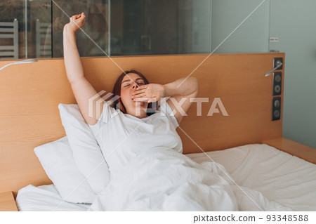 Beautiful redhead Woman waking up in the morning sitting in bed yawning. Good morning. Millennial Caucasian girl wake up in cozy white bed at home or hotel, Eyes closed. 93348588