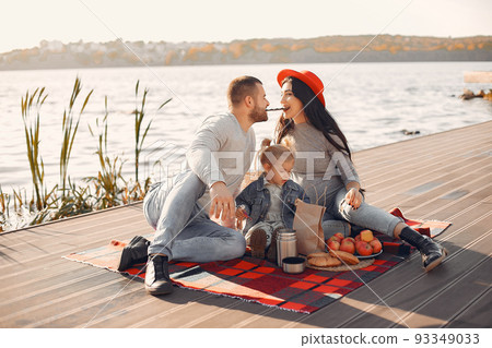 Family in a autumn park. Mother in a red hat. Cute little girl with parent on a picnic Family in a autumn park. Mother in a red hat. Cute little girl with parent on a picnic 93349033