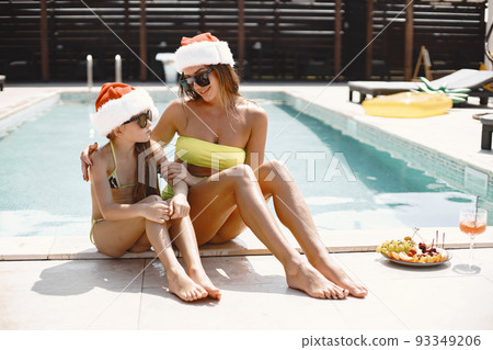 Mother and her daughter wearing Christmas hats by the pool. Have fun. Winter holidays at exotic resort. 93349206