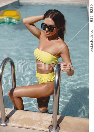 Woman on ladder of the pool at the resort. She looks happy, fashionable and fit in one piece. Woman on ladder of the pool at the resort. She looks happy, fashionable and fit in one piece. 93349229