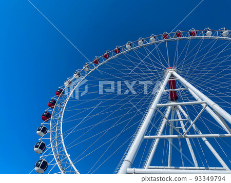 amusement park. ferris wheel made of white metal. a huge wheel with booths for tourists in white and red. ferris wheel against blue clear sky amusement park. ferris wheel made of white metal. a huge wheel with booths for tourists in white and red. ferris wheel against blue clear sky 93349794