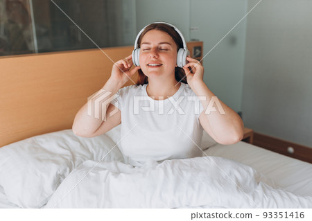 Young Woman enjoying music with wireless headphones, she relaxing in cozy bedroom at home. Enjoy good quality sound, Stress free concept, copy space. Young Woman enjoying music with wireless headphones, she relaxing in cozy bedroom at home. Enjoy good quality sound, Stress free concept, copy space. 93351416