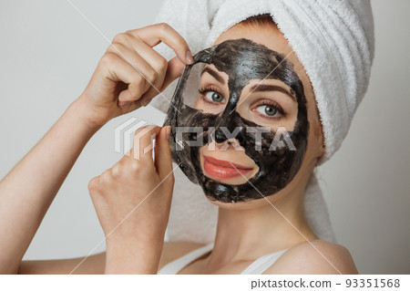 Portrait of smiling young woman removing cosmetic mask from face. 93351568