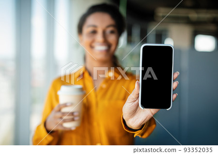 Positive black businesswoman showing modern smartphone with blank empty screen and holding cup, mockup, copy space Positive black businesswoman showing modern smartphone with blank empty screen and holding cup, mockup, copy space 93352035