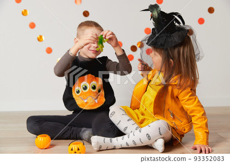 Cute little girl and boy in witch and spider costume play at home. Halloween party Cute little girl and boy in witch and spider costume play at home. Halloween party 93352083