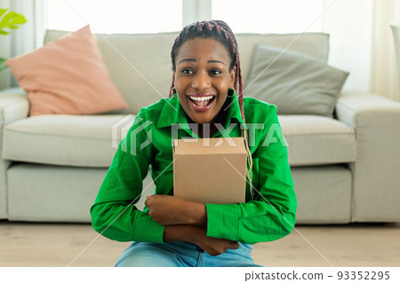 Delivery concept. Overjoyed african american female customer hugging cardboard box package and smiling to camera. 93352295