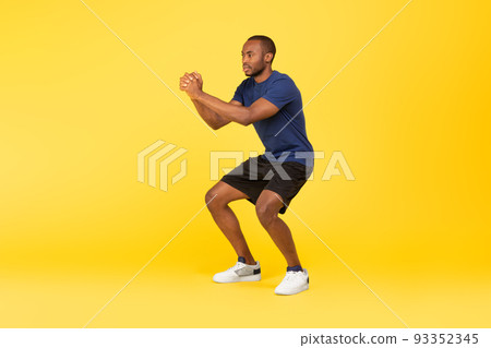Athletic African American Man Doing Deep Squat Exercise, Yellow Background Athletic African American Man Doing Deep Squat Exercise, Yellow Background 93352345