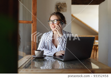 Happy young businesswoman sitting at table with laptop, holding mobile phone call with client in office. Skilled manager saleswoman calling customer, giving professional consultation. 93352458