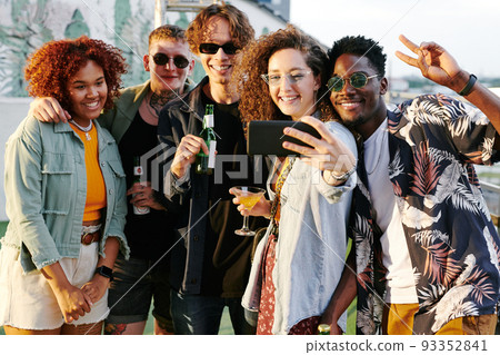 Young cheerfl woman with cocktail in martini glass making selfie with friends 93352841