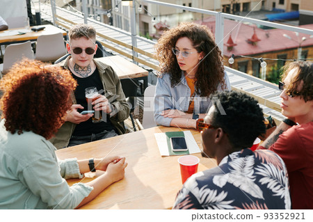 Group of young intercultural friends in casualwear having rest in outdoor cafe 93352921