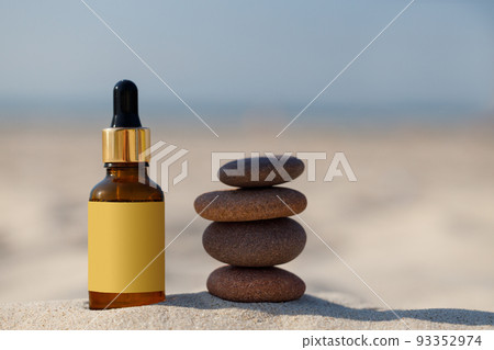 A bottle with a dropper and gold cap on the sand of the beach. Mock-up for a medicinal or cosmetic product, zen stone. A bottle with a dropper and gold cap on the sand of the beach. Mock-up for a medicinal or cosmetic product, zen stone. 93352974