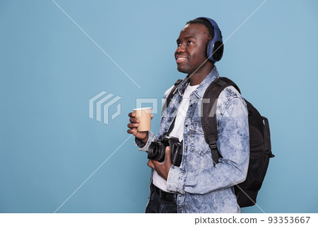 Smiling young man with professional camera and backpack going on holiday trip. Photography enthusiast having DSLR device and wireless headphones going on citybreak vacation. 93353667