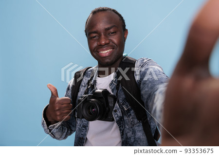 Confident photographer showing okay finger symbol while taking selfie and having DSLR camera on blue background. Photography enthusiast giving approve hand gesture while taking picture of himself. 93353675