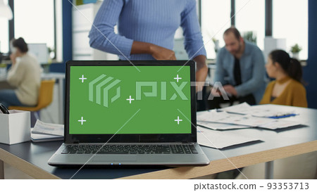 Laptop computer with green screen on desk in front of african american startup employee looking at paper with charts. Focus on portable computer screen with chroma key empty background. Laptop computer with green screen on desk in front of african american startup employee looking at paper with charts. Focus on portable computer screen with chroma key empty background. 93353713
