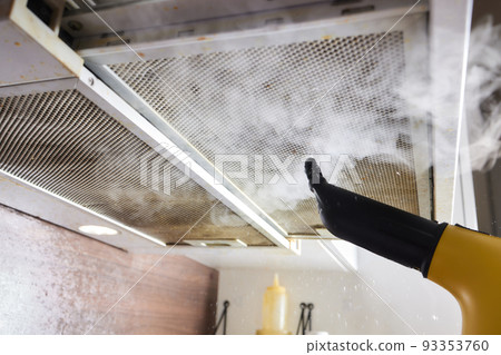 house cleaning. Girl brushes steam cleaners kitchen drawing with steam in green gloves. cleaning of a surface. 93353760
