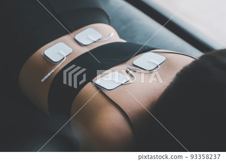 Physical therapy for woman patient with TENS electrode pads on back,Preparing equipment 93358237