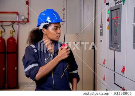 Electrical young asian woman engineer examining maintenance cabinet system electric and using radio. 93358905