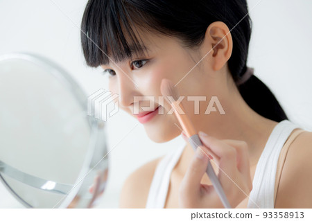 Beautiful young asian woman applying brush on cheek makeup of cosmetic looking mirror on bed. Beautiful young asian woman applying brush on cheek makeup of cosmetic looking mirror on bed. 93358913