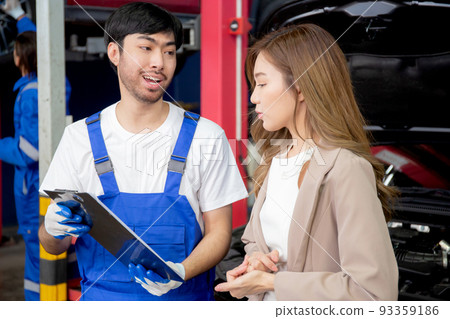 Young mechanic talking to customer asian woman about car with repairing in garage, auto service. 93359186