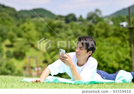 A man operating a smartphone while lying face down on the lawn 93359918
