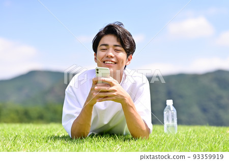 A man operating a smartphone while lying face down on the lawn 93359919
