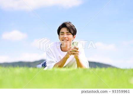 A man operating a smartphone while lying face down on the lawn 93359961