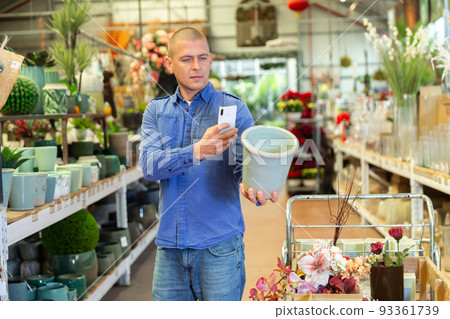 Male shopper scanning qr code on flower pot using smartphone 93361739
