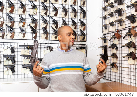 Interested Hispanic man choosing hunting revolver in gun shop 93361748