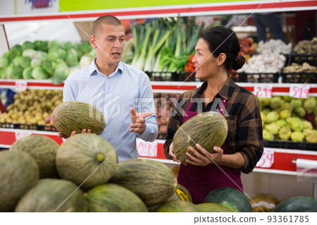 Saleswoman helping male buyer to choose melon in store Saleswoman helping male buyer to choose melon in store 93361785