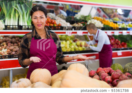 Friendly saleswoman offering fruits and vegetables in greengrocery store Friendly saleswoman offering fruits and vegetables in greengrocery store 93361786