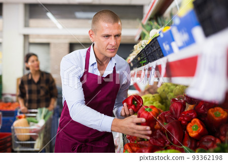 Supermarket worker stacking red peppers Supermarket worker stacking red peppers 93362198