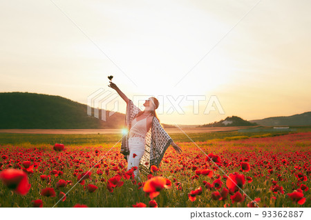 A woman eating strawberries at sunset in a field of poppies. Front view. 93362887
