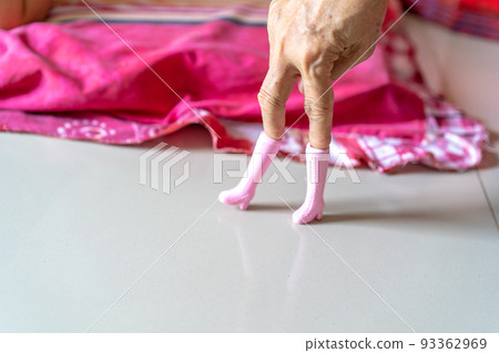 The old woman's hand plays pink plastic boots toy and post it like a model's post. The old woman's hand plays pink plastic boots toy and post it like a model's post. 93362969