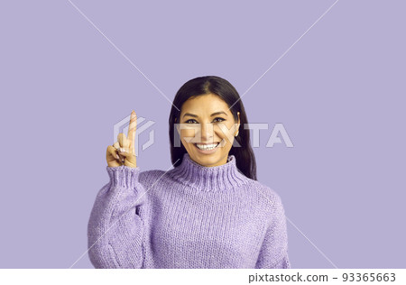 Pretty young female with pleasant smile, makes gesture with index finger, points upwards 93365663