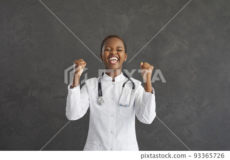 Young African American female doctor sincerely rejoices raising fists and smiling. Young African American female doctor sincerely rejoices raising fists and smiling. 93365726