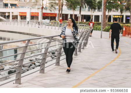 An Indian girl walks along the embankment and talks on the phone. 93366638