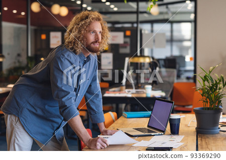 Thoughtful young caucasian businessman with document at desk in creative office Thoughtful young caucasian businessman with document at desk in creative office 93369290