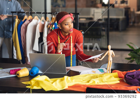 African american fashion designer with document and laptop looking away in studio office African american fashion designer with document and laptop looking away in studio office 93369292