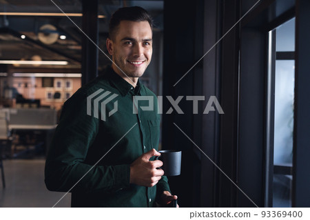 Portrait of smiling caucasian young businessman with coffee cup at creative office Portrait of smiling caucasian young businessman with coffee cup at creative office 93369400
