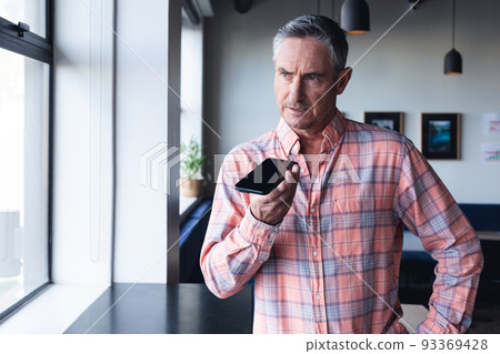Serious caucasian mature businessman talking on smart phone speaker by window at creative office 93369428